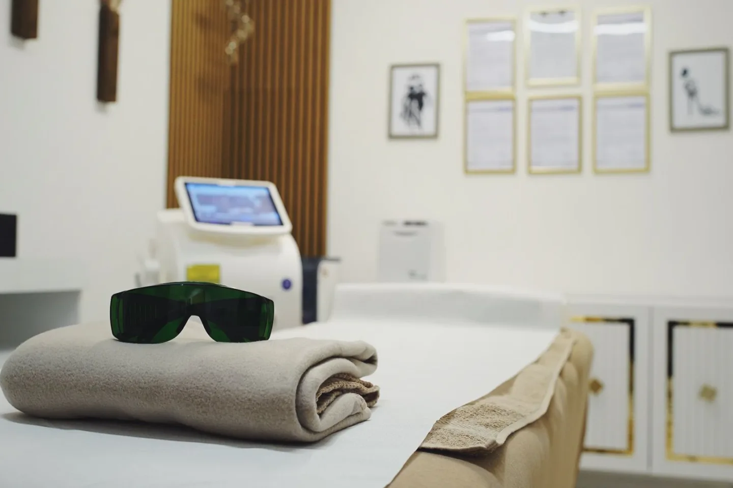 Laserschutzbrille auf einer gefalteten Decke auf der Behandlungsliege, dahinter das Lasergerät für die Haarentfernung