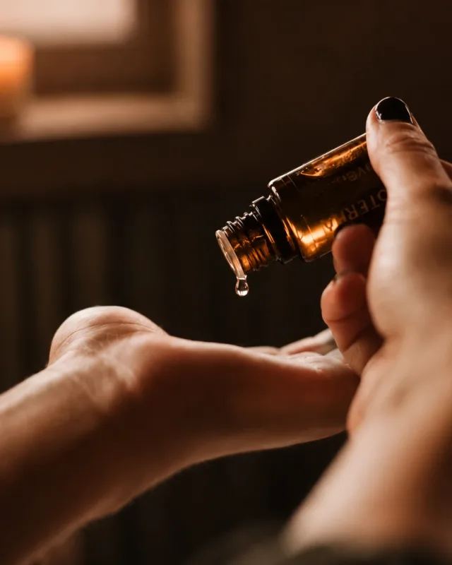 Ein Tropfen Serum fällt aus einer braunen Glasflasche in die Handfläche