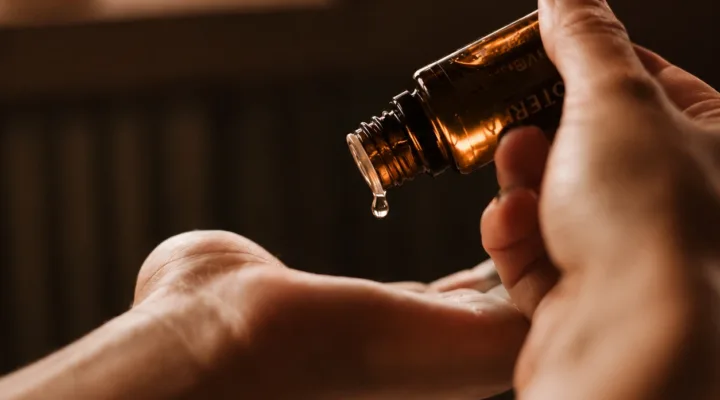 Ein Tropfen Serum fällt aus einer braunen Glasflasche in die Handfläche